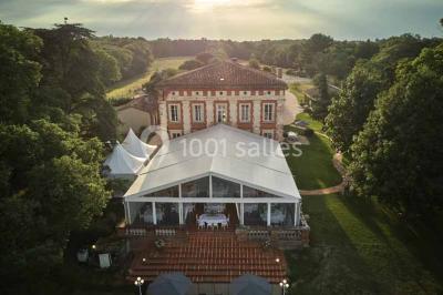 Vue aérienne d'un domaine entouré de forêts et de champs au coucher du soleil, avec des bâtiments et des allées visibles.