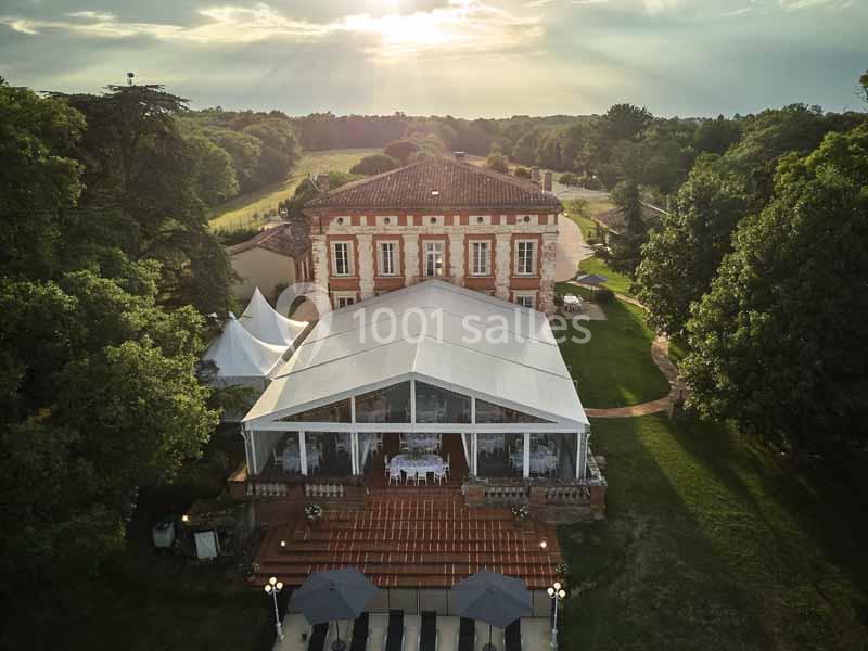 Vue aérienne d'un bâtiment historique entouré de verdure, avec une grande structure transparente installée devant.