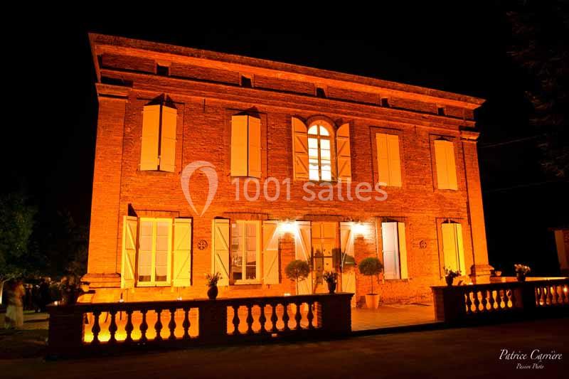 Façade d'une maison en briques rouges éclairée par des lumières chaudes dans un environnement nocturne.