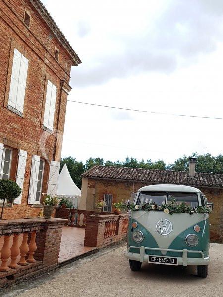Un van vintage décoré de fleurs est garé devant une maison en briques rouges avec une terrasse.