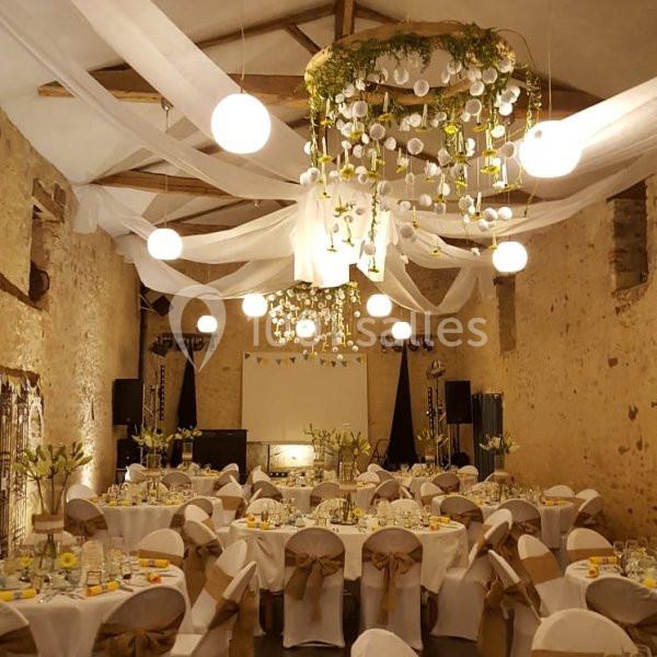 Salle de réception décorée avec des tables rondes, des chaises ornées de nœuds et un plafond agrémenté de voilages et…