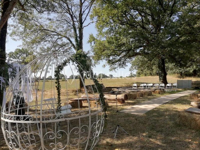 Espace extérieur aménagé pour un événement, avec des bottes de foin, des chaises blanches et une structure métallique…