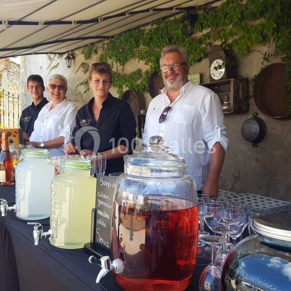 Quatre personnes souriantes derrière un stand proposant des boissons en carafes sous un auvent.