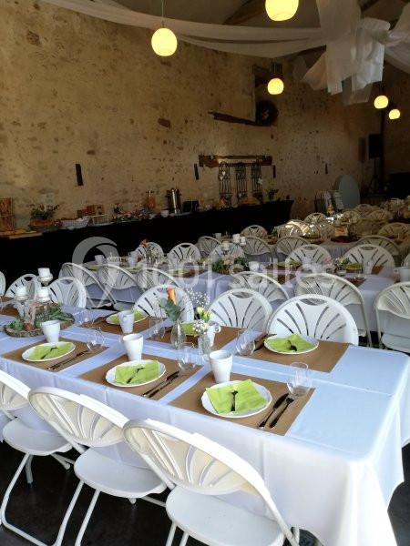 Salle de réception décorée avec des tables dressées, nappes blanches, chaises pliantes et centres de table fleuris.