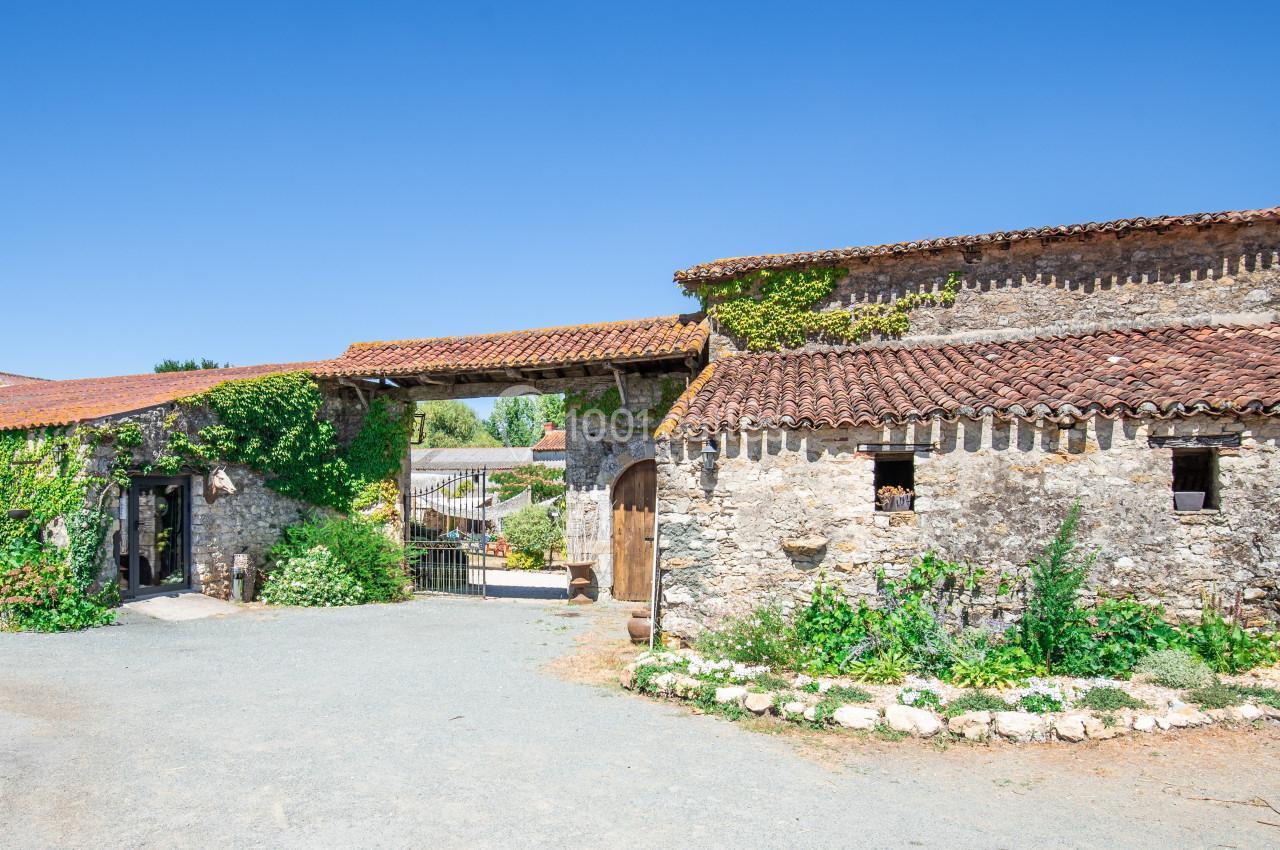 Bâtiments en pierre avec toits en tuiles rouges, entourés de végétation, sous un ciel bleu clair.