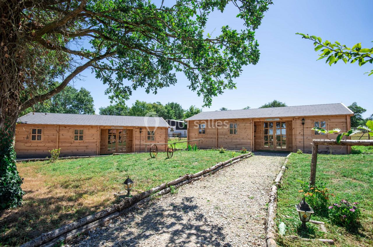 Chemin en gravier menant à des chalets en bois entourés de pelouse et d'arbres sous un ciel dégagé.