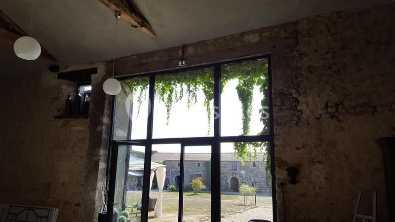 Grande baie vitrée avec vue sur une cour extérieure, encadrée de murs en pierre et ornée de plantes tombantes.