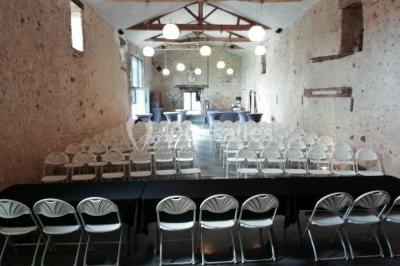 Salle de réception décorée avec des tables dressées, nappes blanches, chaises pliantes et centres de table fleuris.