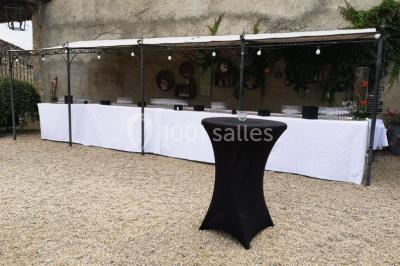 Salle de réception décorée avec des tables dressées, nappes blanches, chaises pliantes et centres de table fleuris.
