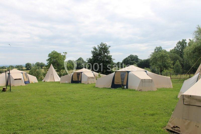 Tentes beige installées sur une pelouse verte, entourées d'arbres sous un ciel partiellement nuageux.