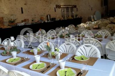 Salle de réception décorée avec des tables dressées, nappes blanches, chaises pliantes et centres de table fleuris.