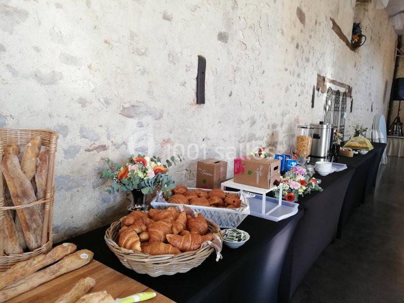 Buffet avec viennoiseries, baguettes, boissons chaudes, céréales et décorations florales sur une table dans une salle en…