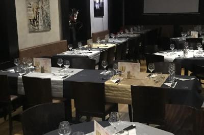 Table de restaurant dressée avec nappes noires et grises, verres, couverts, serviettes pliées et menu au centre.