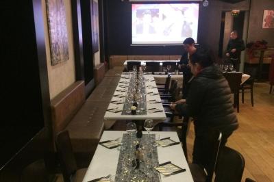 Table de restaurant dressée avec nappes noires et grises, verres, couverts, serviettes pliées et menu au centre.