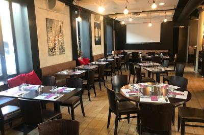 Table de restaurant dressée avec nappes noires et grises, verres, couverts, serviettes pliées et menu au centre.