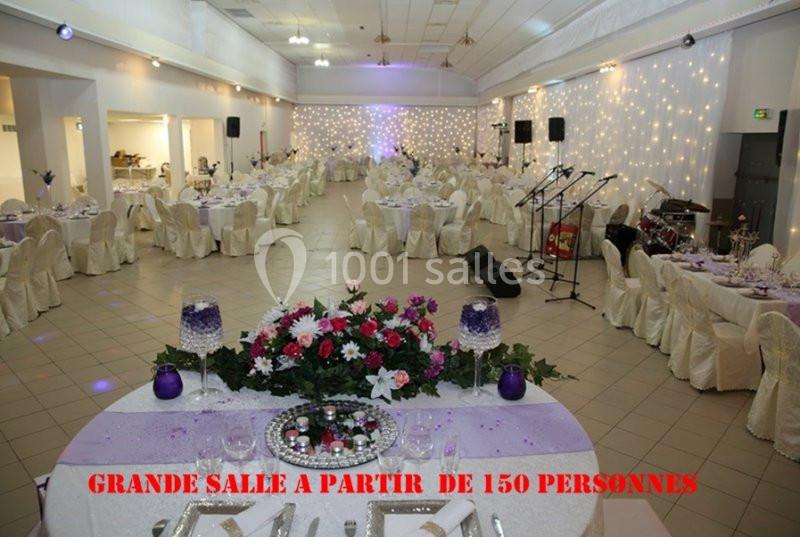 Salle de réception décorée avec des tables rondes, nappes blanches, éclairage tamisé et espace pour la musique.