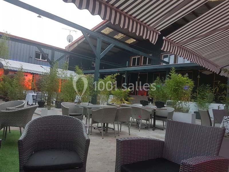 Terrasse extérieure avec mobilier en rotin, tables et chaises, entourée de bambous et protégée par des stores rayés.