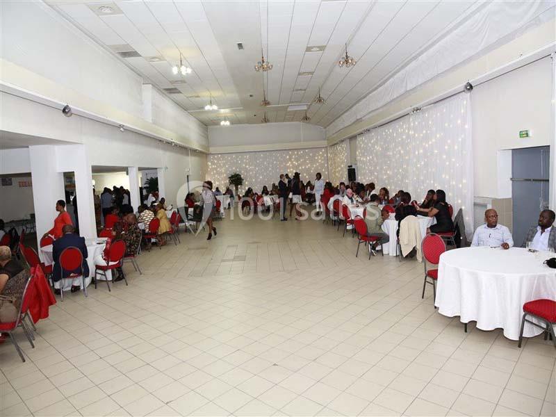 Salle de réception avec des invités assis à des tables rondes, éclairée par des guirlandes lumineuses au fond.