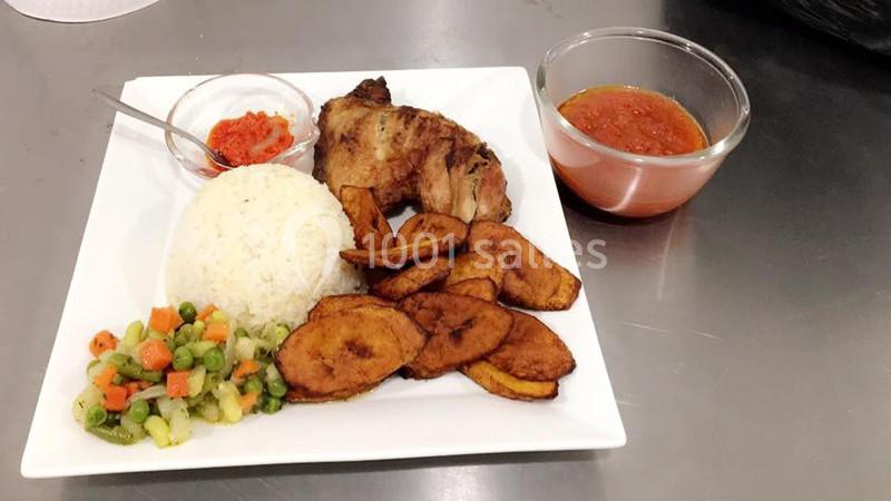 Assiette contenant du riz, poulet grillé, bananes plantains frites, légumes sautés et sauces en accompagnement.