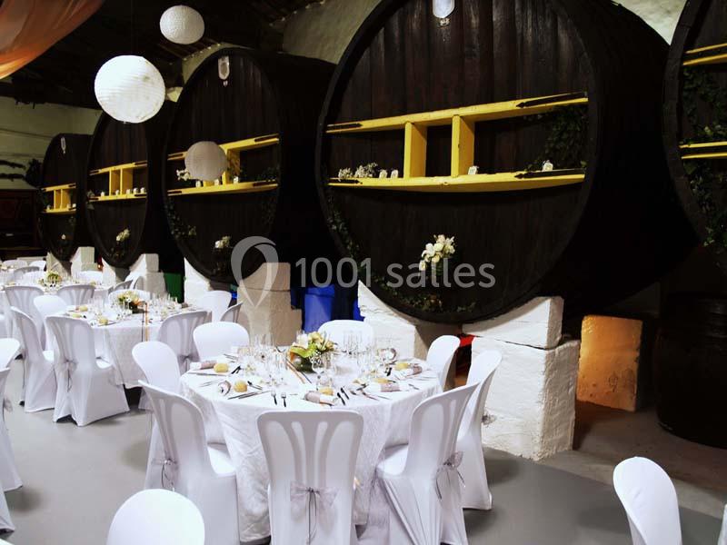 Salle de réception décorée avec des tables rondes dressées et des tonneaux en bois en arrière-plan.