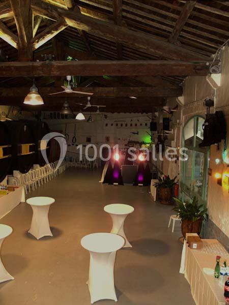 Salle de réception avec tables hautes, chaises alignées le long des murs et éclairage tamisé.