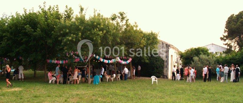 Groupe de personnes rassemblées dans un jardin sous des arbres décorés de guirlandes colorées, près de bâtiments.