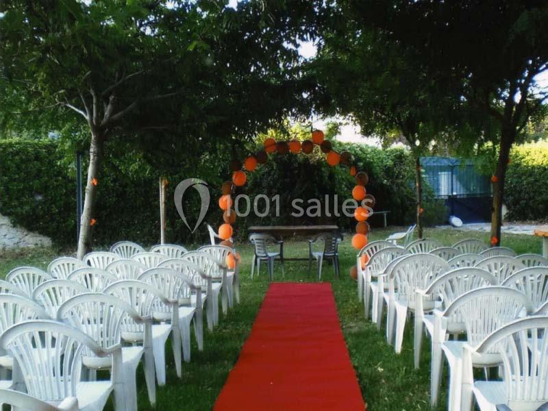 Chaises blanches disposées en rangées de part et d'autre d'une allée rouge menant à une arche décorée de ballons orange.