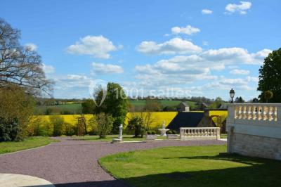 Miniature Location salle Préaux-Bocage (Calvados) - Domaine d'Aslan #21 Paysage rural avec un chemin en gravier, des champs de colza jaunes, des arbres et une terrasse en pierre au premier plan.