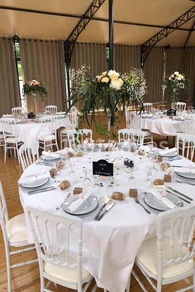 Salle de réception décorée avec des tables rondes dressées, nappes blanches et compositions florales élégantes.