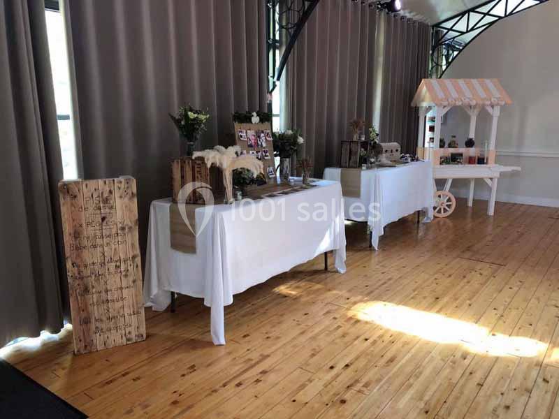 Tables décorées avec nappes blanches, fleurs et objets rustiques dans une salle lumineuse au sol en bois.