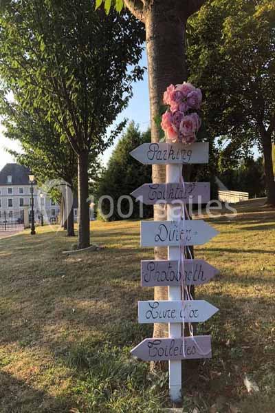 Panneau directionnel en bois avec flèches indiquant parking, cocktail, dîner, photobooth, livre d'or et toilettes.