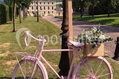 Miniature Location salle Préaux-Bocage (Calvados) - Domaine d'Aslan #11 Paysage rural avec un chemin en gravier, des champs de colza jaunes, des arbres et une terrasse en pierre au premier plan.