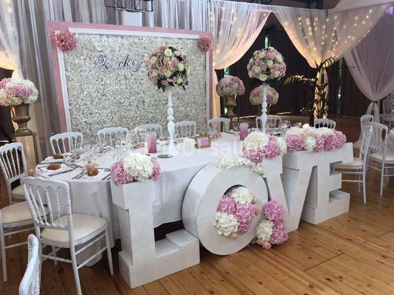 Table de réception décorée avec des fleurs roses et blanches, entourée de chaises blanches et ornée du mot ’LOVE’ en grand.