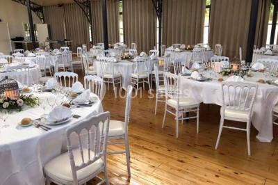 Miniature Location salle Préaux-Bocage (Calvados) - Domaine d'Aslan #4 Paysage rural avec un chemin en gravier, des champs de colza jaunes, des arbres et une terrasse en pierre au premier plan.