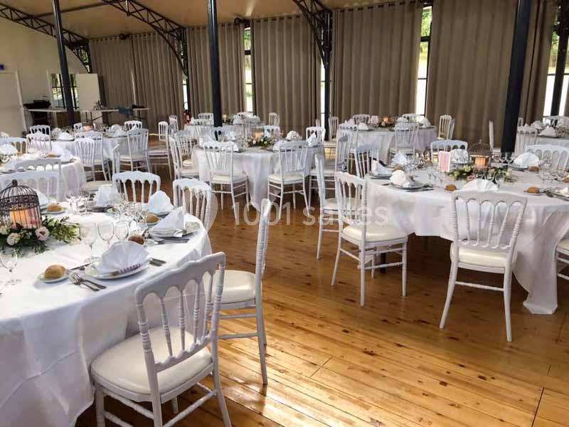 Salle de réception avec tables rondes dressées, nappes blanches, chaises élégantes et décoration florale.