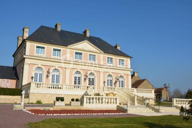 Grande maison de style classique avec façade rose, balustrades blanches et jardin bien entretenu sous un ciel bleu.