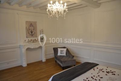 Chambre élégante avec lit double, lustre, murs décorés de papier peint sombre et vue sur un jardin par la fenêtre.
