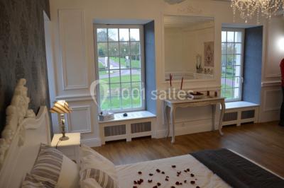 Chambre élégante avec lit double, lustre, murs décorés de papier peint sombre et vue sur un jardin par la fenêtre.