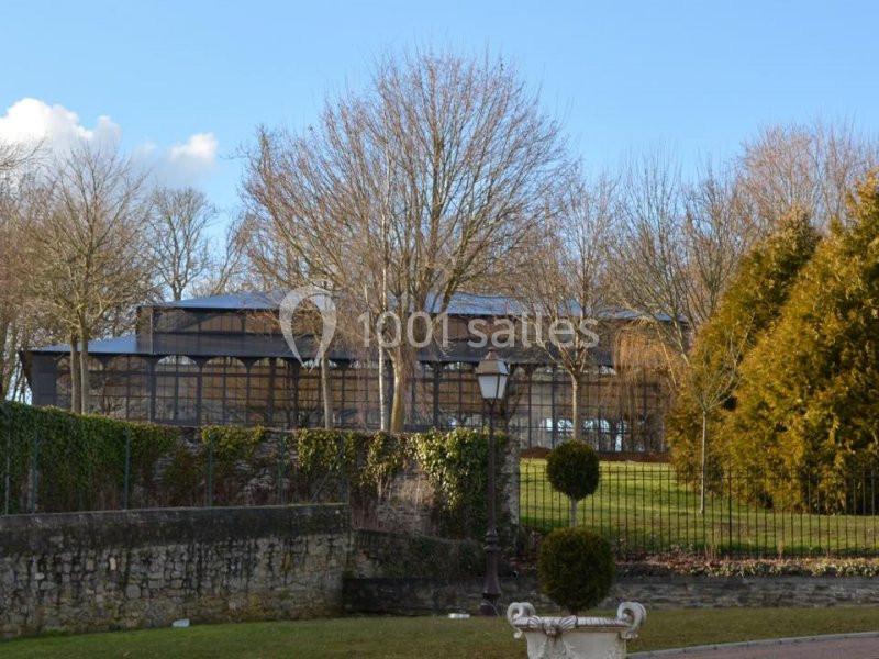 Serre en verre entourée d'arbres dénudés en hiver, avec un lampadaire et un jardin aménagé au premier plan.
