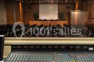 Salle de réunion avec une grande table en bois, chaises noires, parois vitrées et vue sur des immeubles.