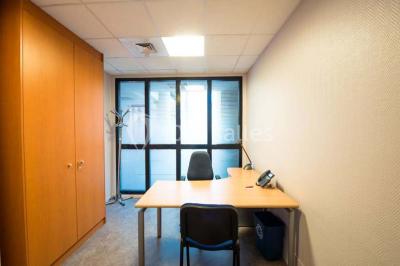 Salle de réunion avec une grande table en bois, chaises noires, parois vitrées et vue sur des immeubles.