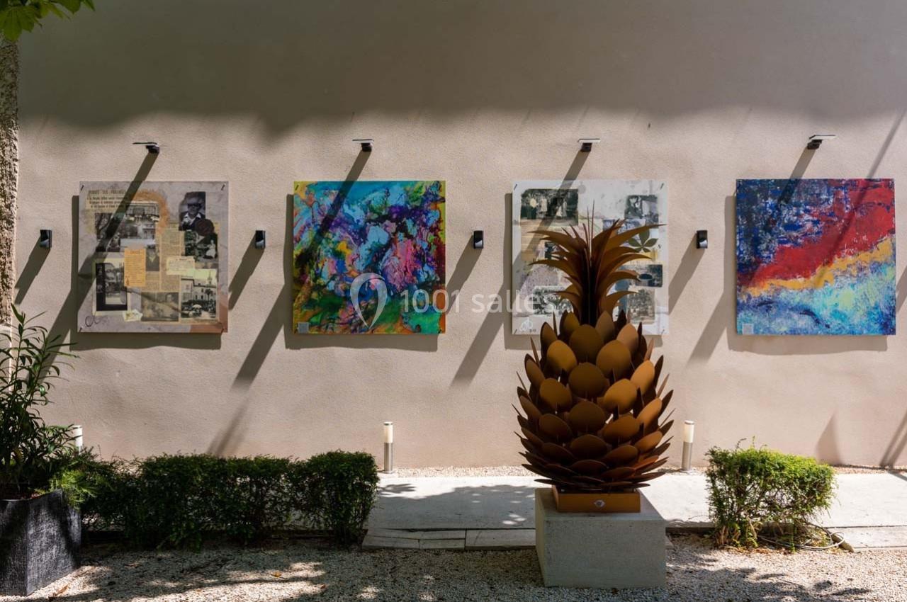 Quatre tableaux colorés accrochés à un mur beige, avec une sculpture en forme d'ananas au premier plan.