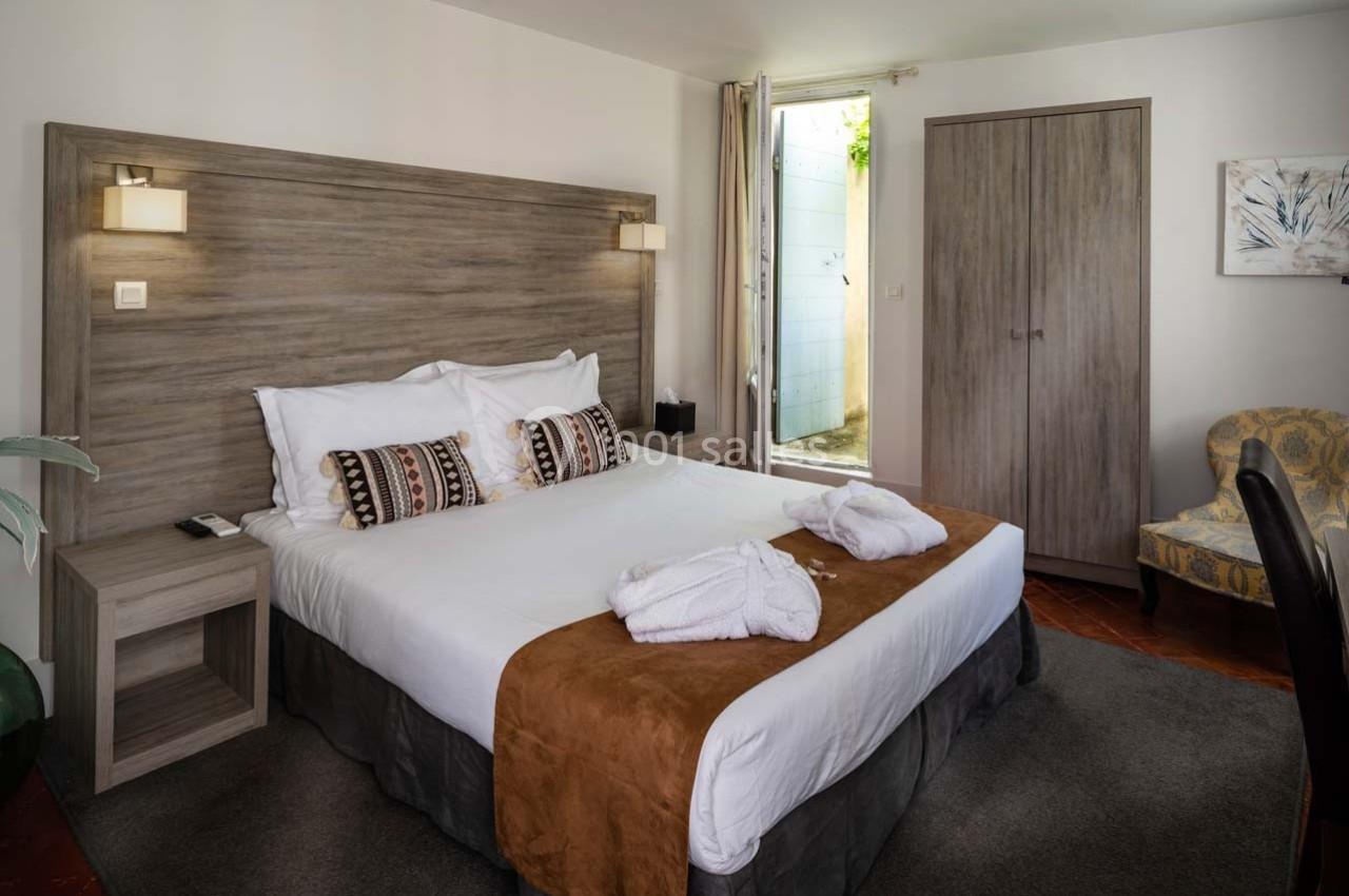 Chambre lumineuse avec lit double, tête de lit en bois, peignoirs posés, armoire et fauteuil dans un décor sobre.