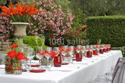 Massif de fleurs rouges et violettes entouré d'arbres et de verdure dans un jardin ensoleillé.
