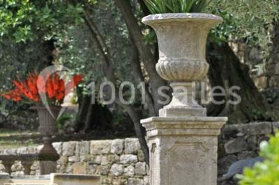 Massif de fleurs rouges et violettes entouré d'arbres et de verdure dans un jardin ensoleillé.