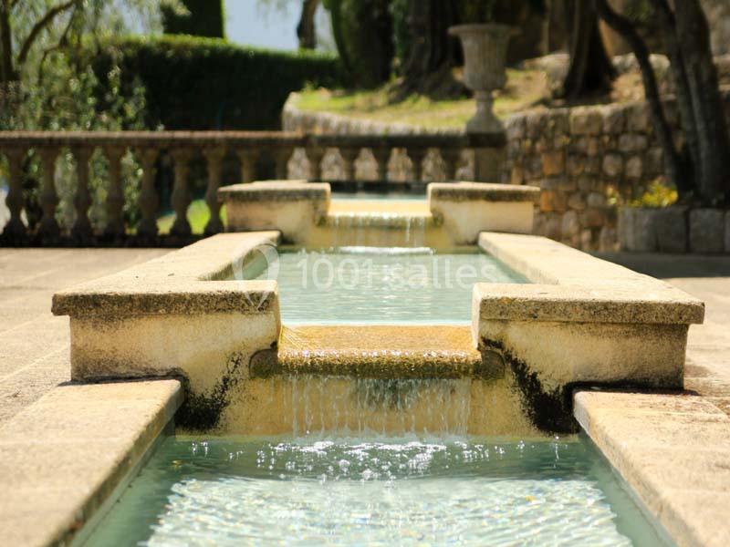 Fontaine en pierre avec plusieurs niveaux d'eau en cascade, entourée de végétation et de murs en pierre.