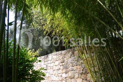 Massif de fleurs rouges et violettes entouré d'arbres et de verdure dans un jardin ensoleillé.