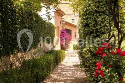 Massif de fleurs rouges et violettes entouré d'arbres et de verdure dans un jardin ensoleillé.