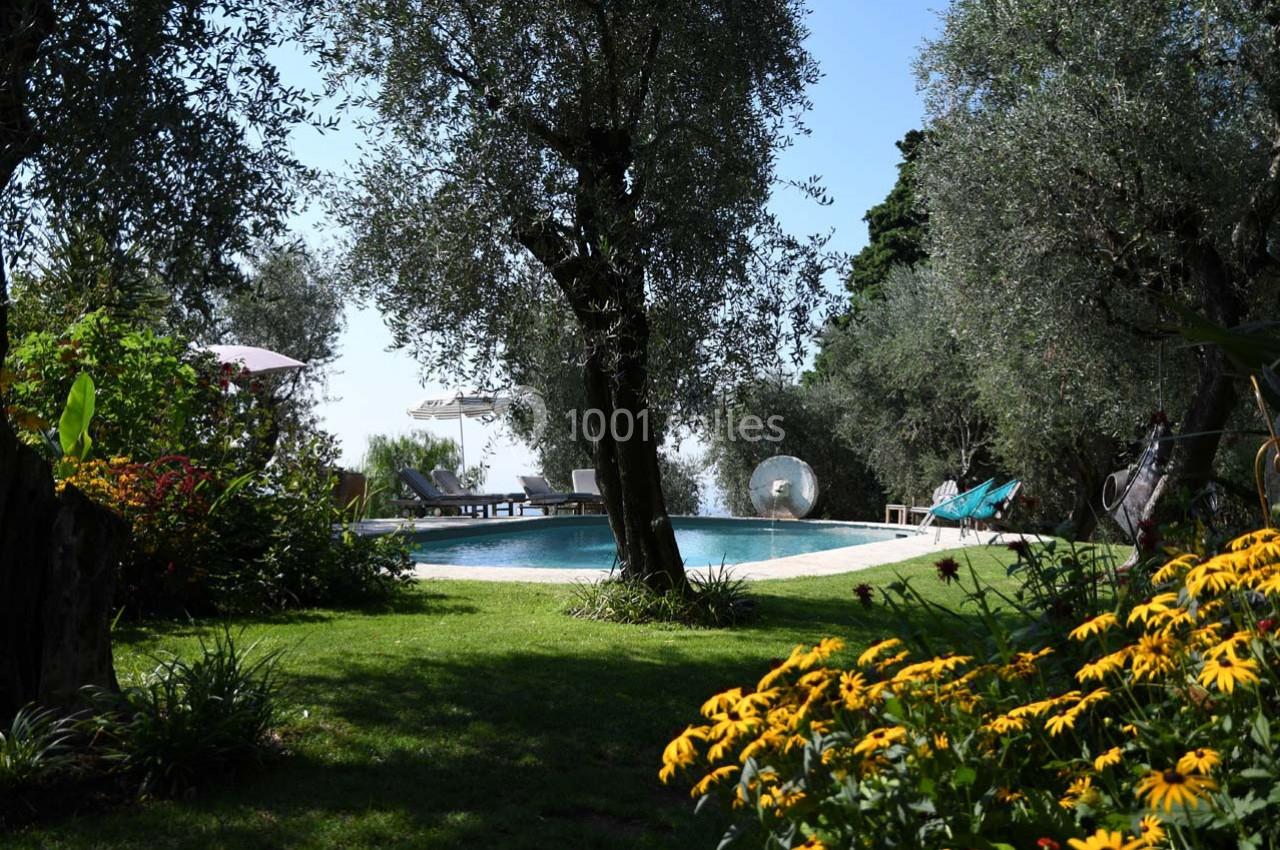 Jardin verdoyant avec des arbres et des fleurs entourant une piscine extérieure sous un ciel dégagé.