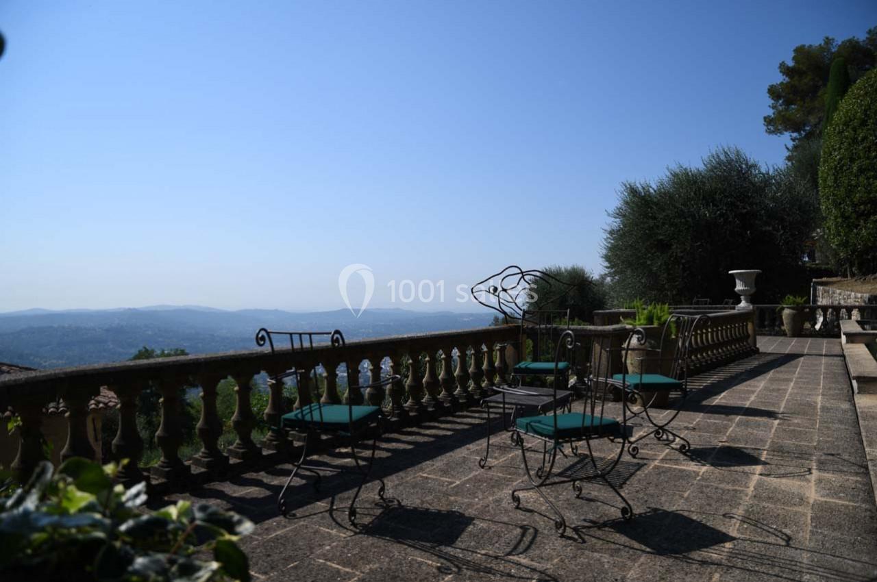Terrasse en pierre avec mobilier en fer forgé, surplombant un paysage vallonné sous un ciel dégagé.